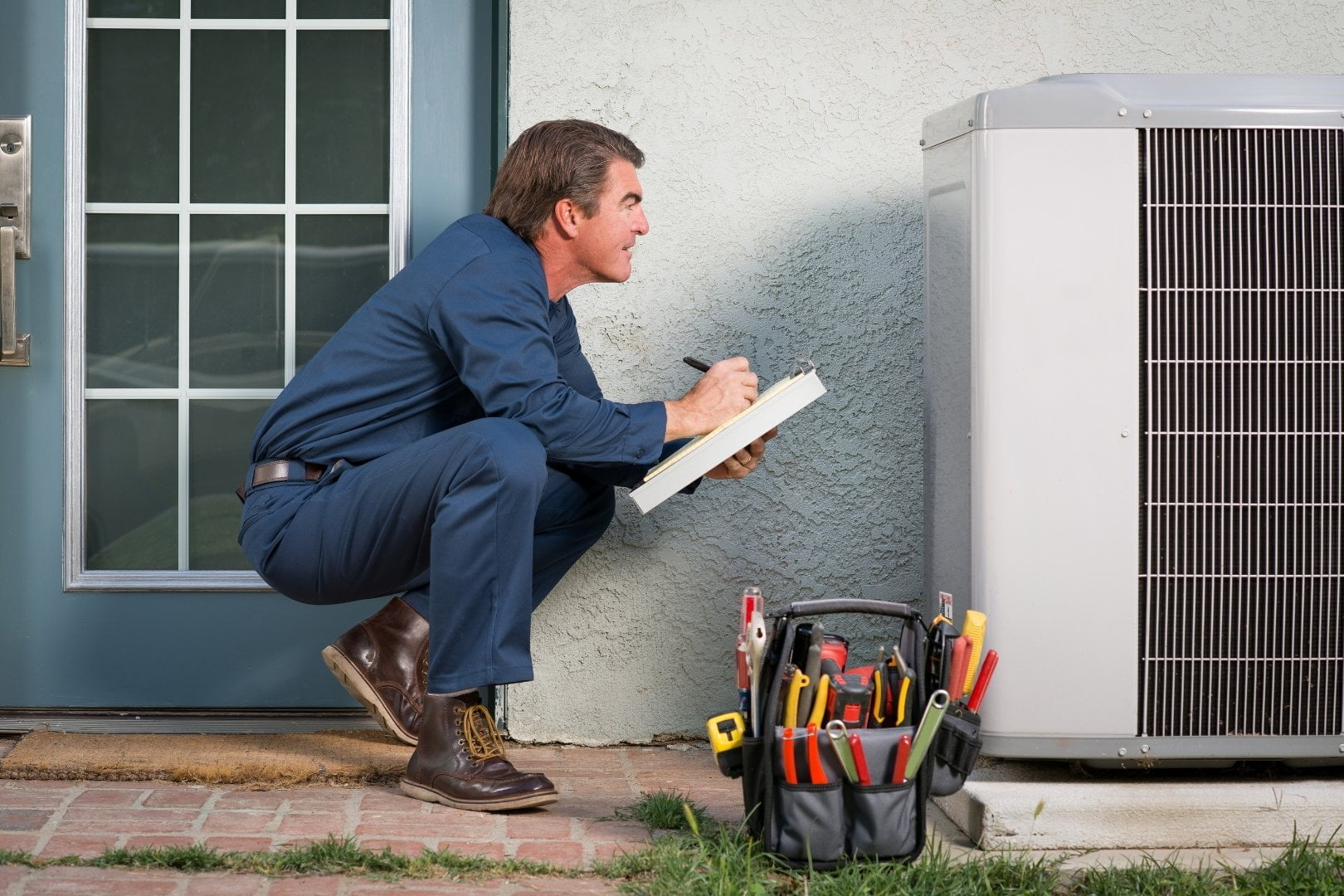 A man fixing an air conditioner outside a home.