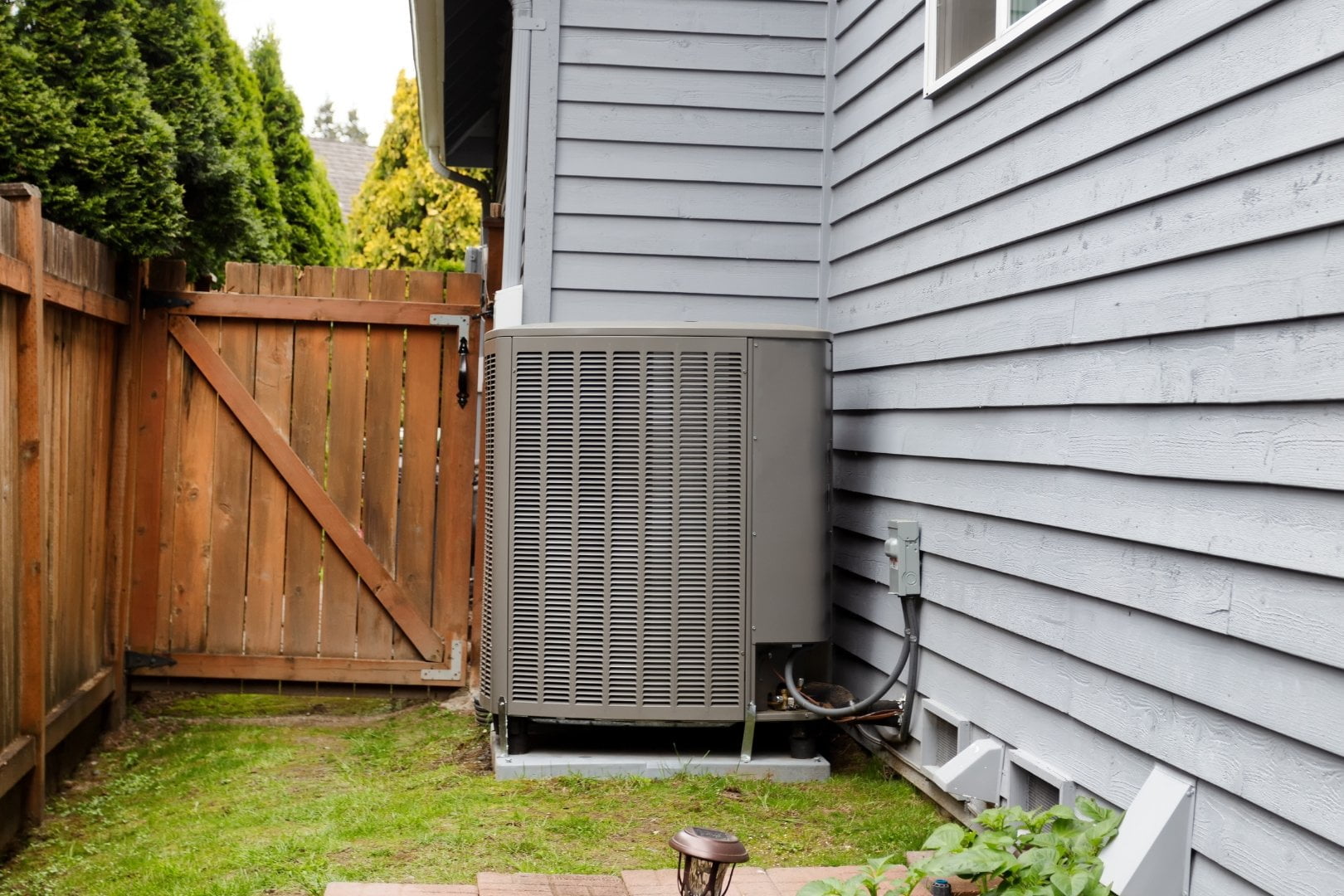 An air conditioning unit REQUIRING maintenance services in the backyard of a house.