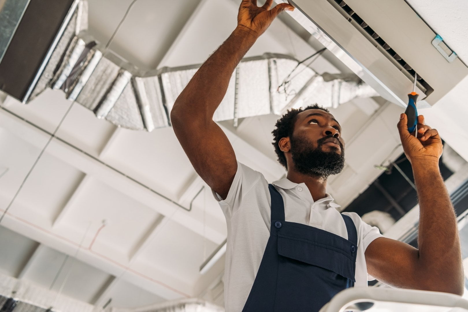 A black man providing commercial HVAC services on an air conditioner.