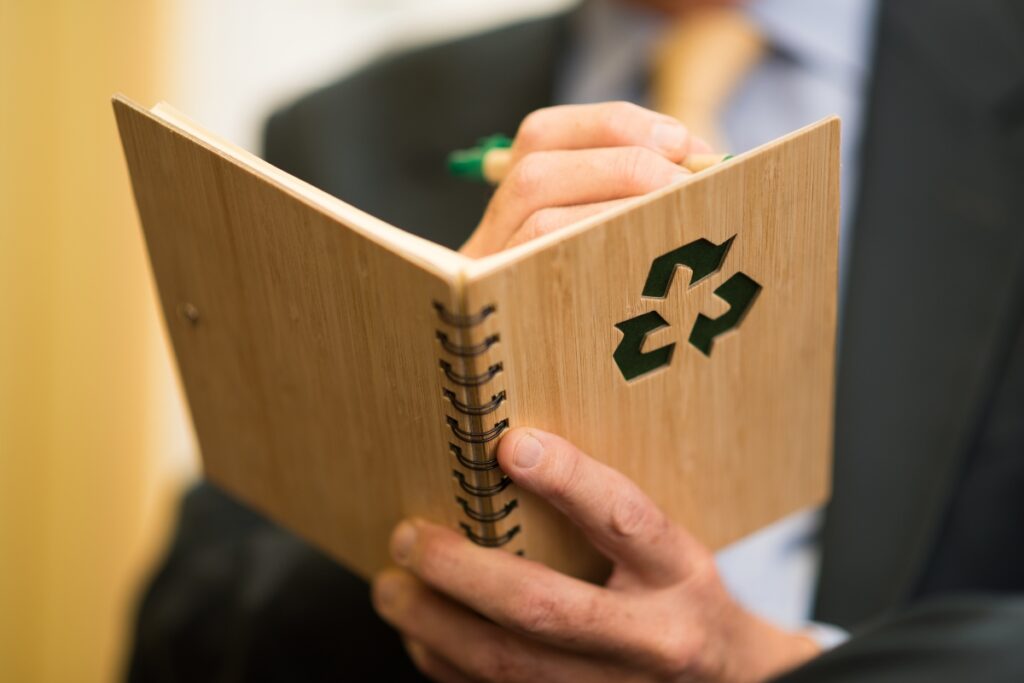         A man in a suit holding a notebook with a recycle symbol on it, sharing energy-saving tips for businesses.