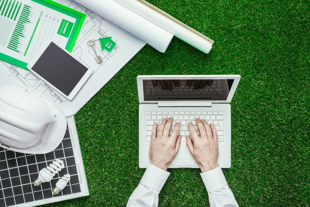 A man is using a laptop on a green grass while implementing energy-saving tips for businesses.