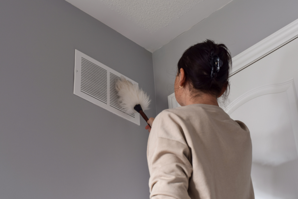A woman performing winter HVAC maintenance by cleaning a vent in a room.