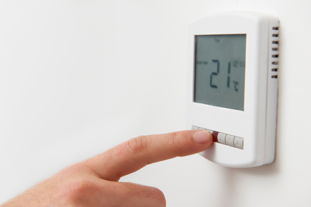 A person is pointing at a thermostat on a wall during winter HVAC maintenance.