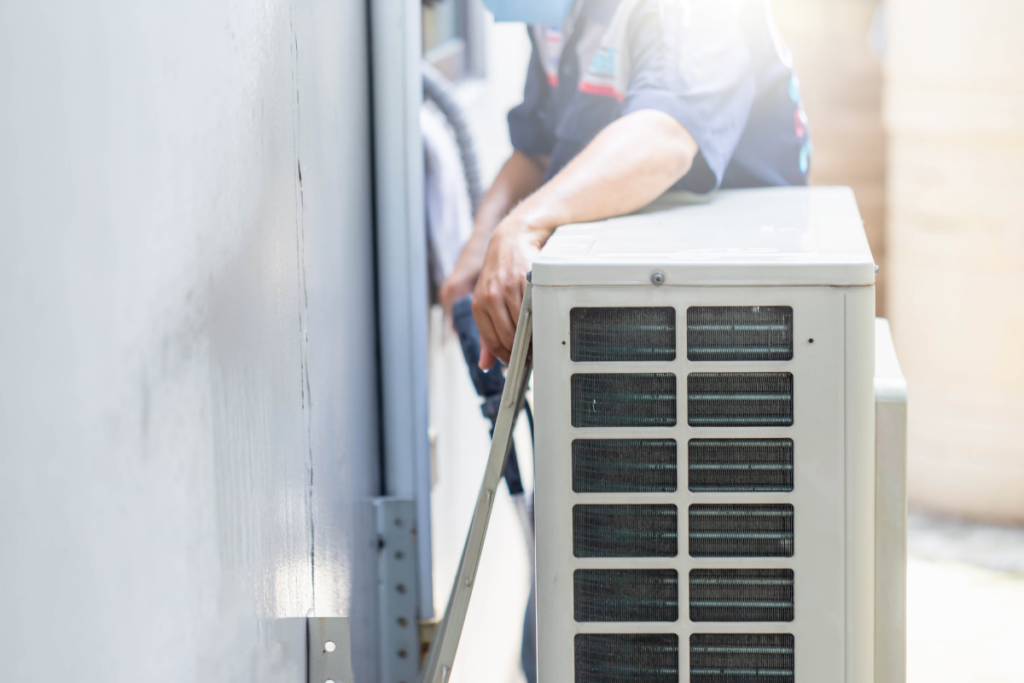 During winter, a man conducts HVAC maintenance while standing next to an air conditioner.
