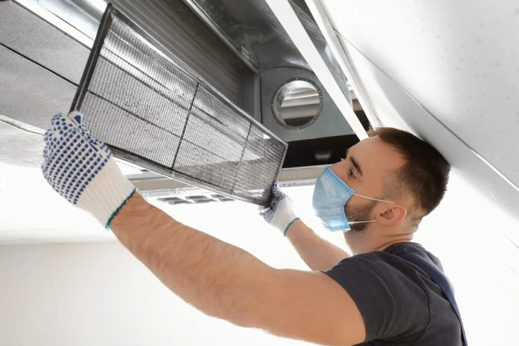A man wearing gloves holding a vent, ensuring HVAC air quality.