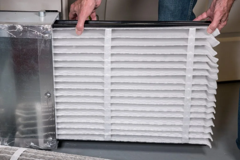 A person's hand holding a white filter for HVAC air quality.