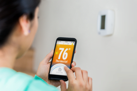 A woman utilizing a smart HVAC system with her phone.