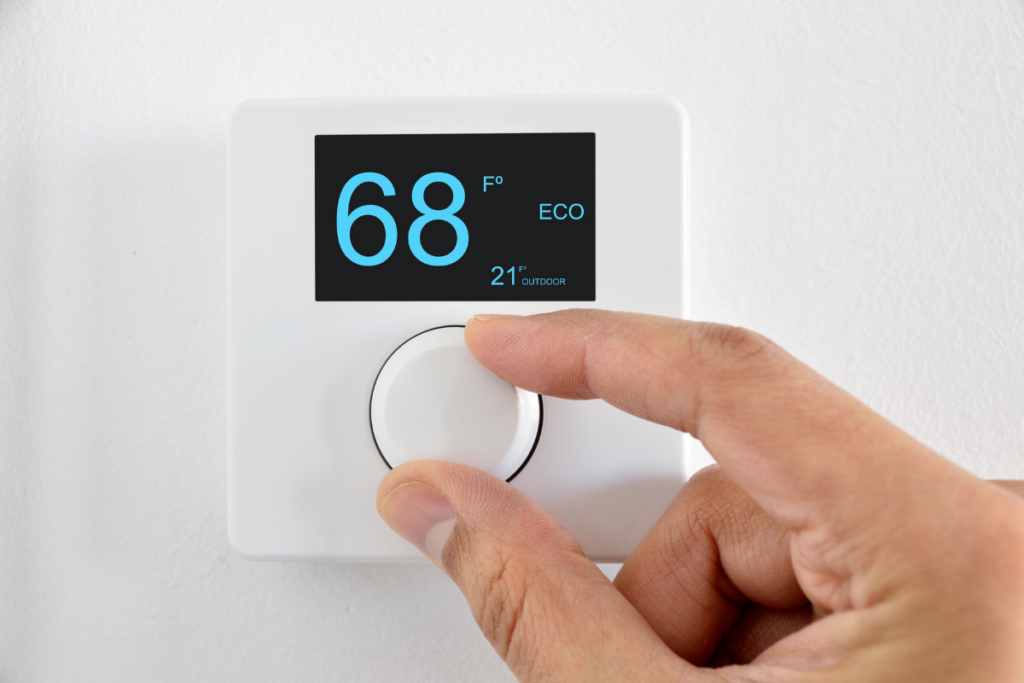 In the winter, a person is adjusting the temperature on an HVAC thermostat as part of their maintenance routine.