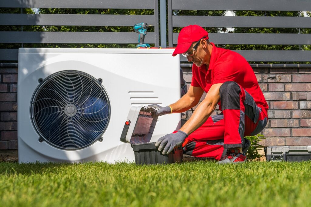 Technician in red uniform servicing an outdoor air conditioning unit with diagnostic equipment in Georgia's climate.