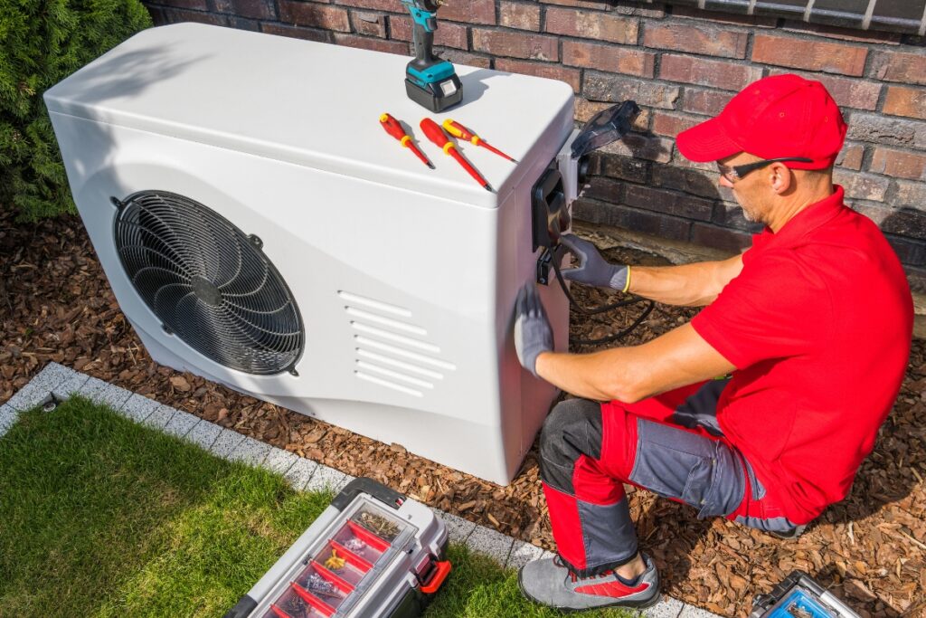 A technician in a red cap and uniform addressing common HVAC issues while servicing an outdoor air conditioning unit with tools nearby.