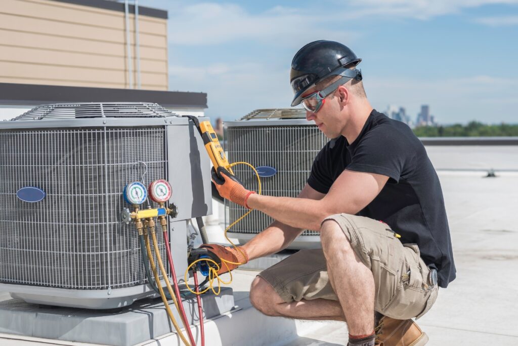 A technician wearing safety gear examines and tests an outdoor HVAC unit on a rooftop during the day, ensuring compliance with HVAC building codes.