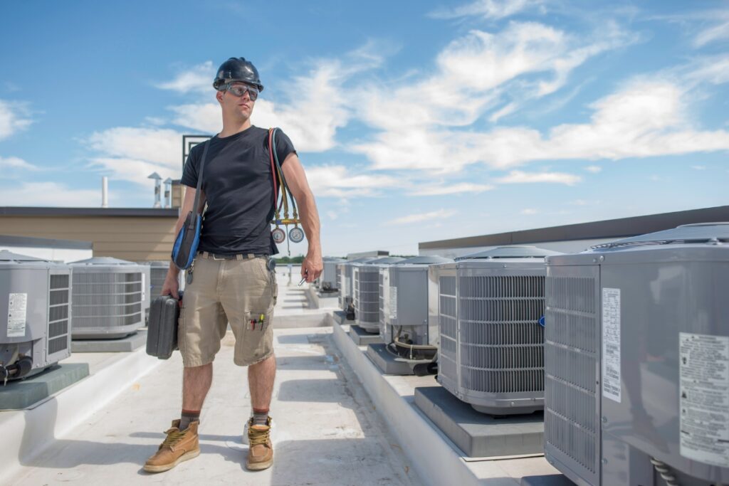 A man stands on a roof surrounded by air conditioners, ensuring everything complies with HVAC building codes.