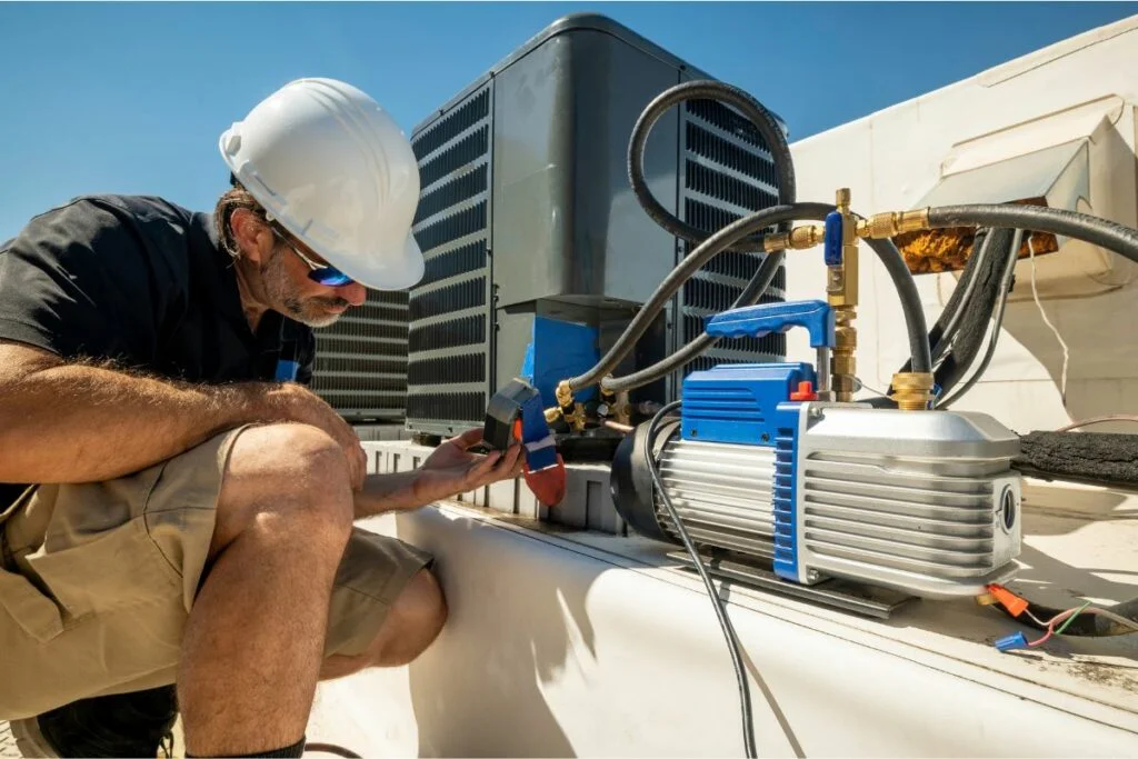 A technician wearing a hard hat tests and chooses the right HVAC system for air conditioning units on a rooftop using specialized equipment.