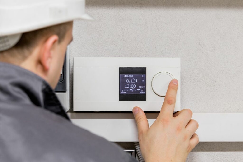 Person in a hard hat adjusting a digital thermostat on a wall, demonstrating how to make renewable energy at home more efficient.