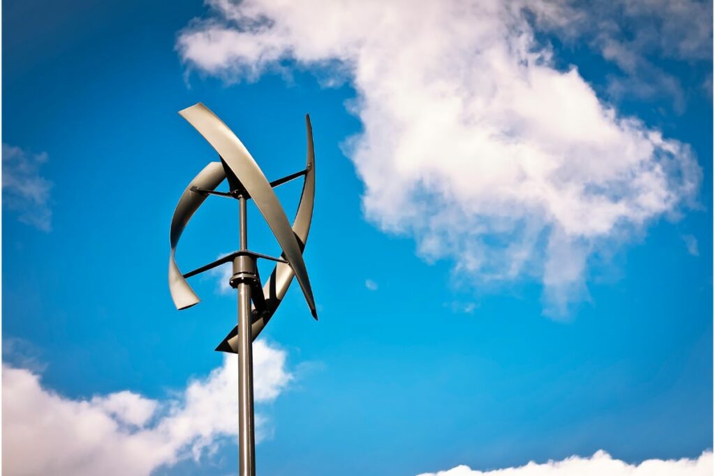 Vertical-axis wind turbine against a backdrop of blue sky with scattered clouds, showcasing how to make renewable energy at home.