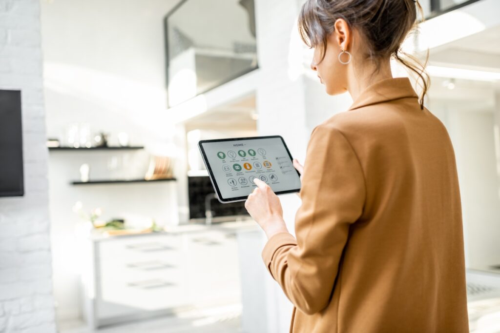 Person using a tablet to control smart home HVAC and other devices in a modern kitchen.