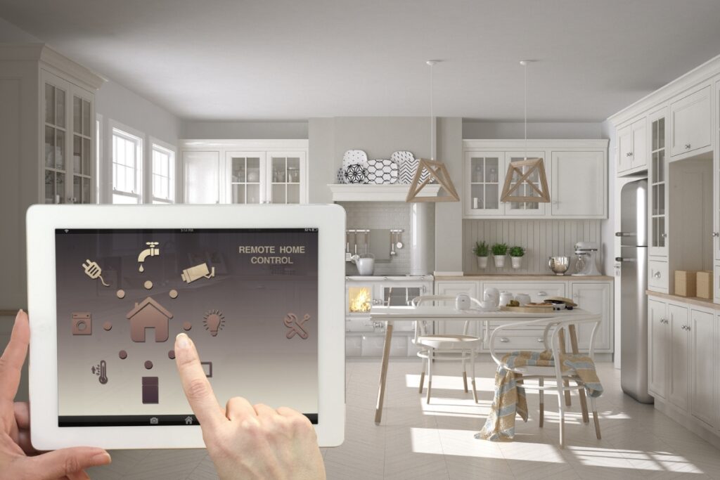 Person using a tablet for remote home control of the smart home HVAC system in a modern kitchen with white cabinetry, a center island, and wooden decor accents.