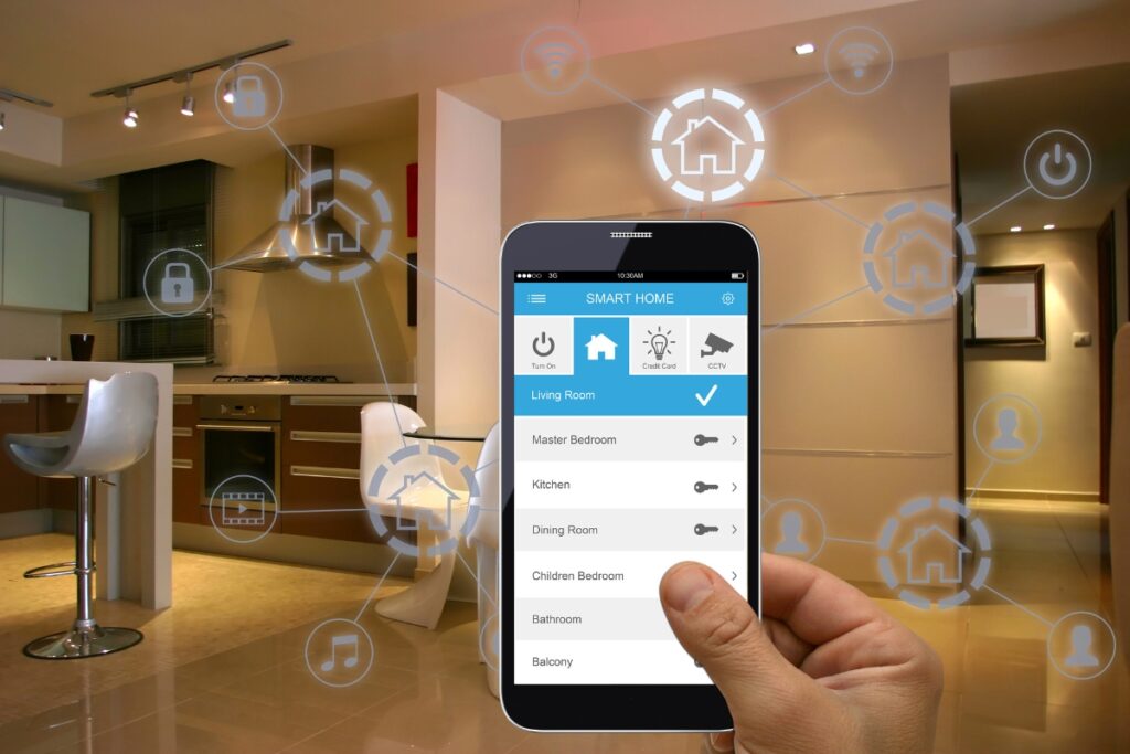 A hand holds a smartphone displaying a smart home control app, with virtual icons for various home functions, including smart home HVAC, overlaying a modern kitchen and living area in the background.