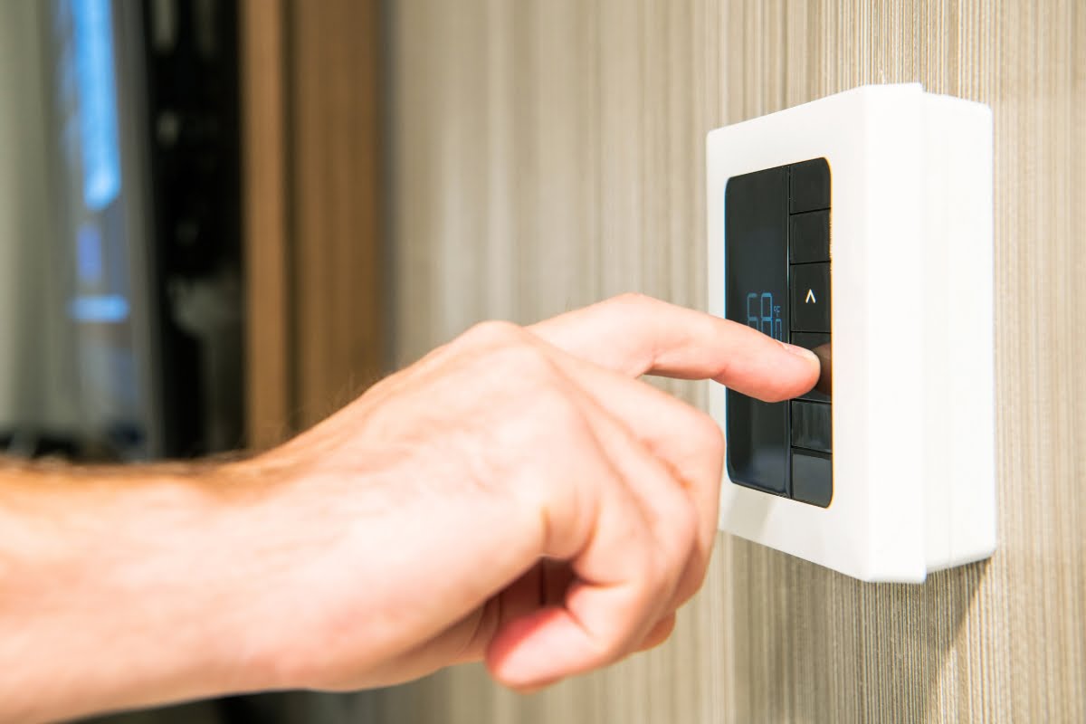 Close-up of a hand adjusting a digital thermostat on a wall, ensuring a healthy home and optimal HVAC performance.