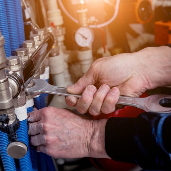 A plumber from a reliable Heating and Air Company in Atlanta is working on a pipe with a wrench.