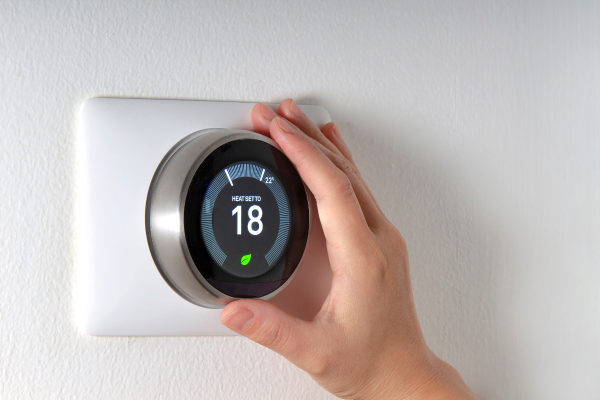 A person is holding a thermostat on a wall, demonstrating their commitment to energy efficiency in HVAC.