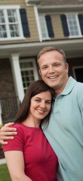 A couple posing in front of a house, highlighting discounts.