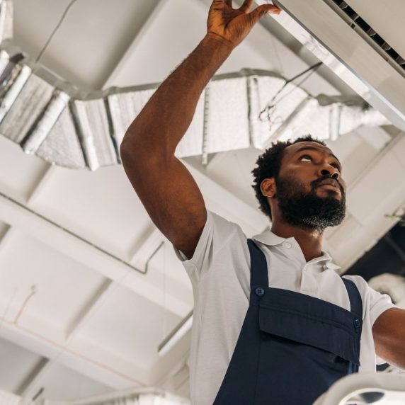 A black man providing commercial HVAC services on an air conditioner.